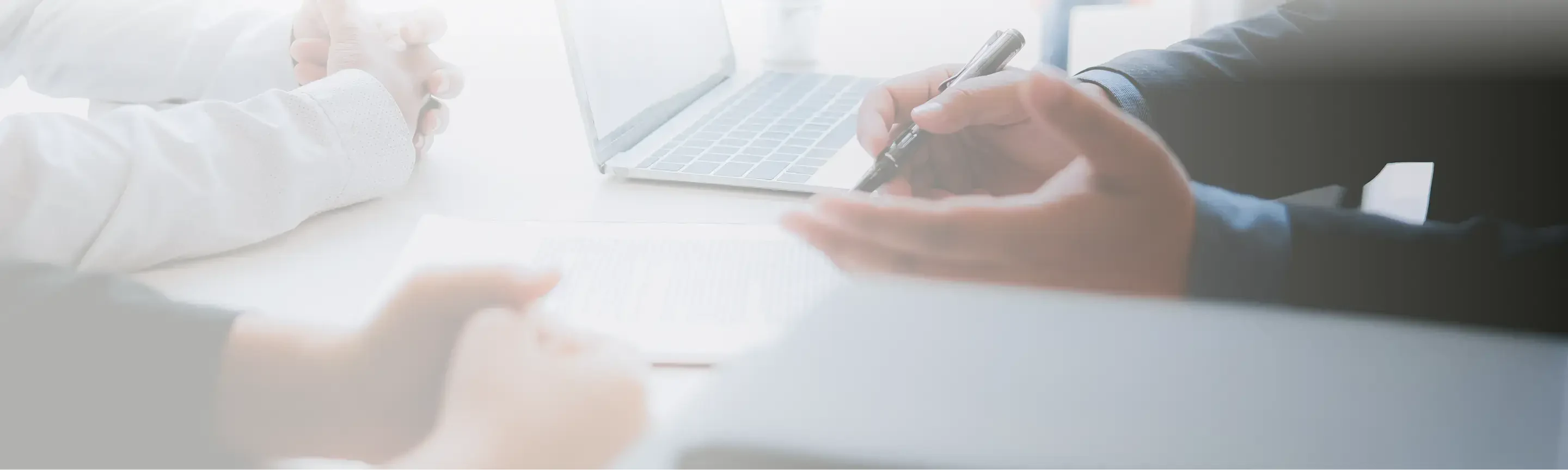 Close-up of hands during a business meeting, with a laptop and documents on the table, emphasizing collaboration and discussion.