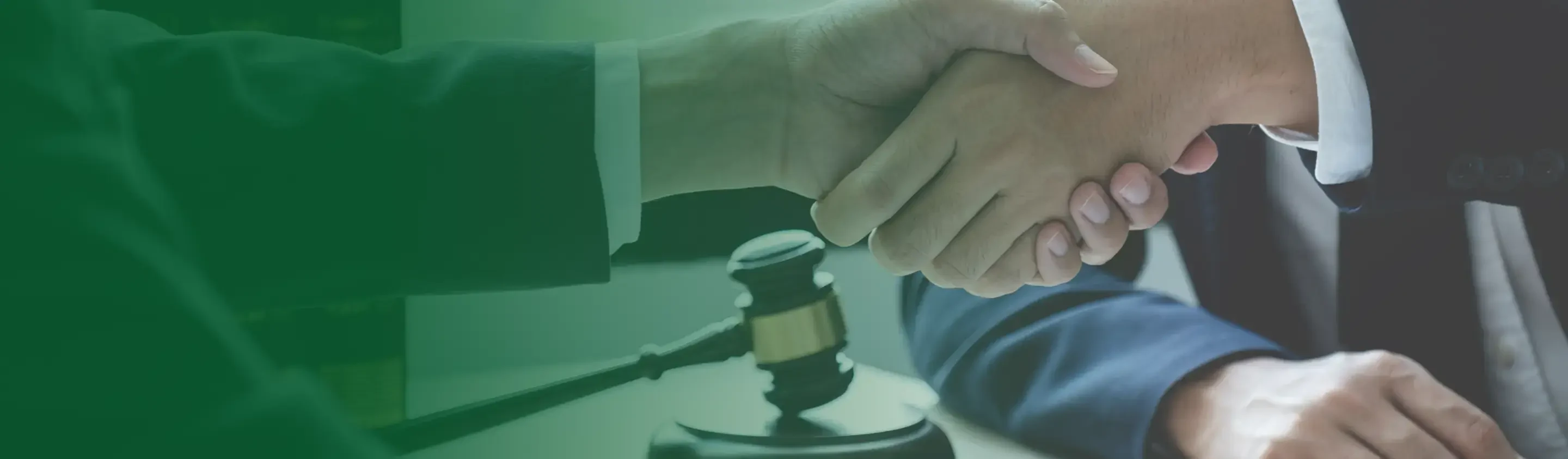 Two individuals wearing suits shake hands firmly, with a gavel visible in the foreground, symbolizing a legal agreement.